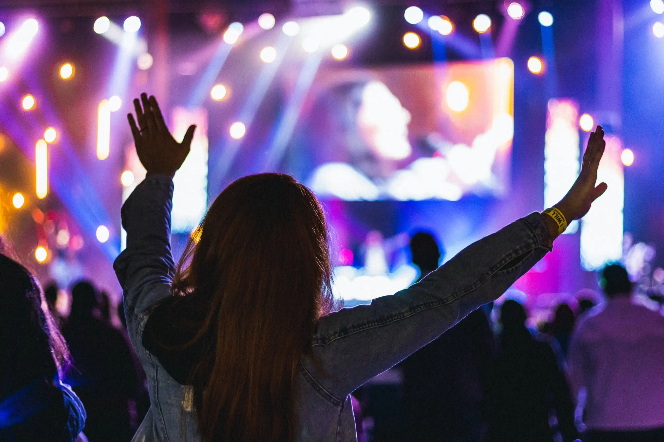 Woman with hands raised in worship under dramatic stage lights